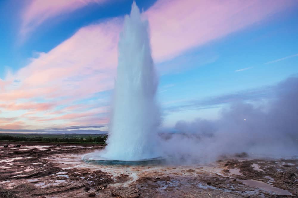 Strokkur Geyser erupting into a pink and blue sunset sky.