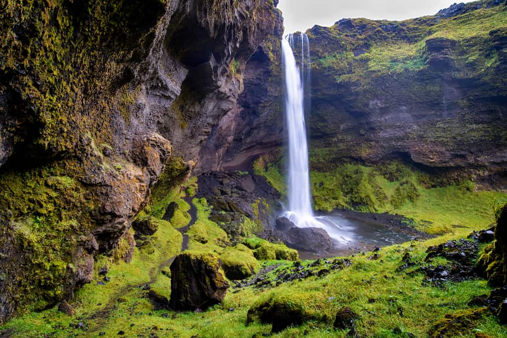 Kvernufoss waterfall flowing over rugged and mossy cliffs into a pool.