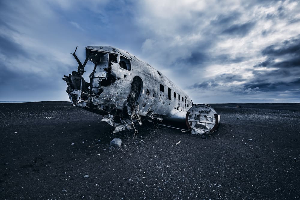 Moody photo of the plane wreck on a black sand beach.