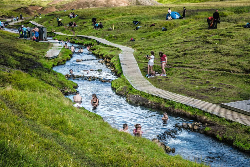People bathing in Reykjadalur Hot Springs with a boardwalk nearby.