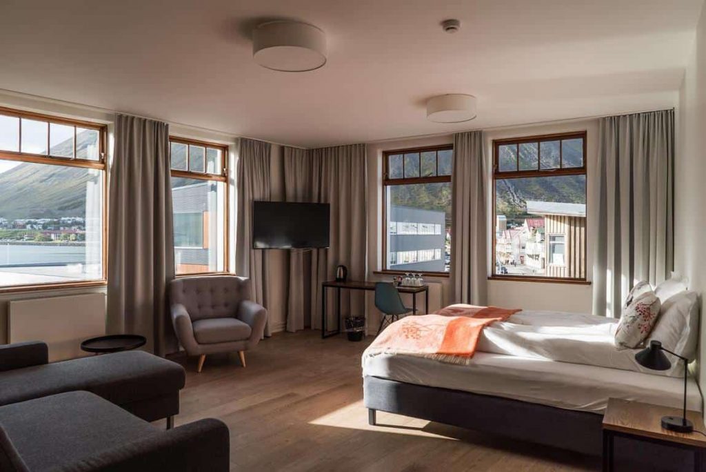 a nice hotel room with a wood floor f windows and nice light coming in.