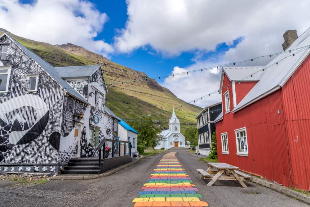 rainbow bricks leading to a light colored church and a mountain in the background on a sunny day