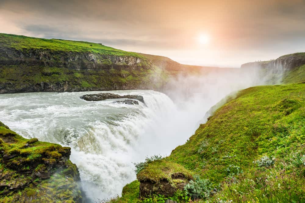 raging gullfoss waterfall in iceland with green grass surrounding it on a sunny evening  