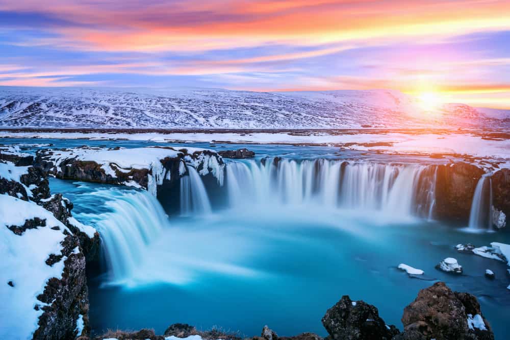 large waterfall surrounded by snow and ice at sunset 