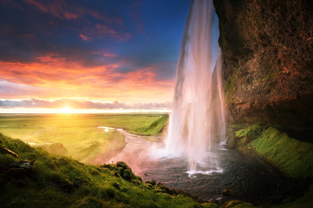 side angle of a waterfall flowing from mountain and a vast landscape in the distance at sunset