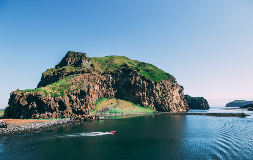 a red boat in the water speeding with a large mountain on the shore on a sunny day