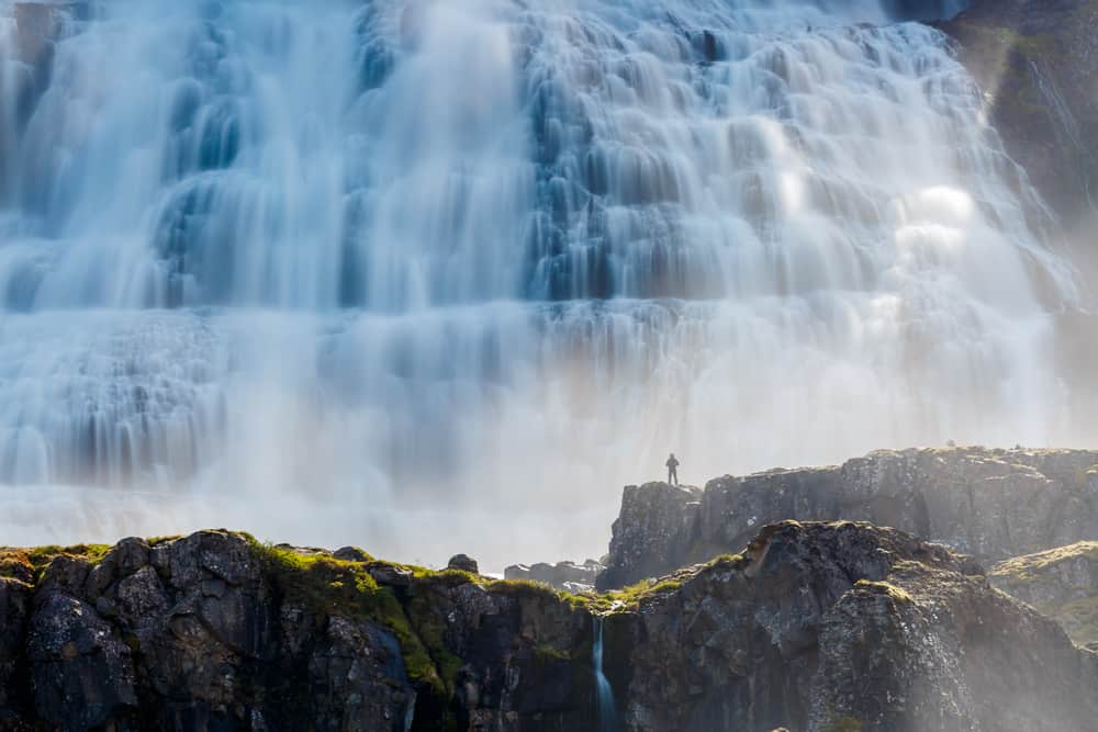 a massive waterfall with a person small in the frame standing on rocks