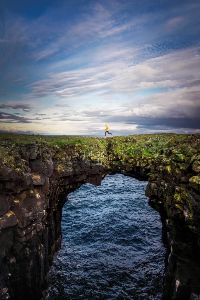 A person running across greenery covered rock sea arch.