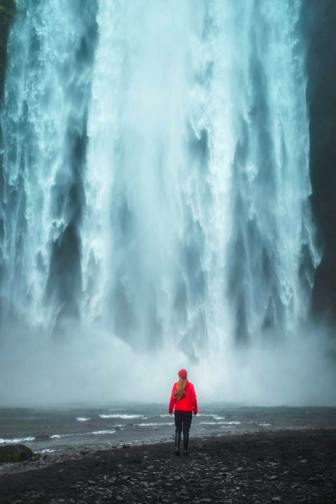 A woman in red at the base of a powerful waterfall in Iceland