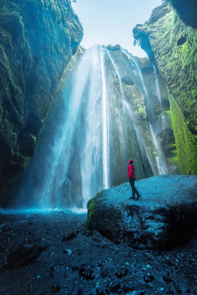 A person in red raincoat standing at base of Gljufrabui waterfall, one of the best things to do in Iceland.