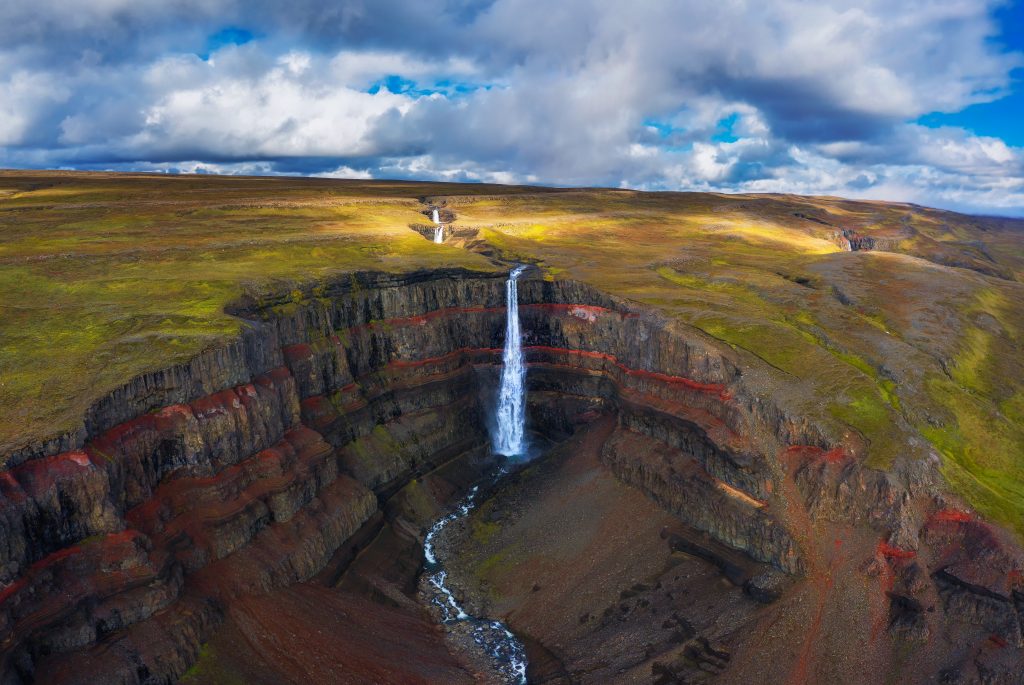 aerial shot of waterfall flowing into canyon lined with red