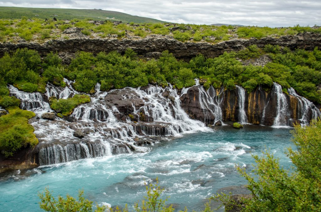 Short waterfall with many streams surrounded by greenery and ending in turquoise pool