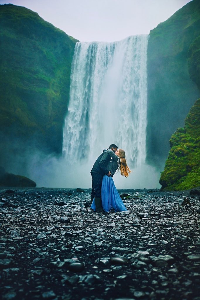 Couple kissing in front of Skogafoss waterfall in Iceland.