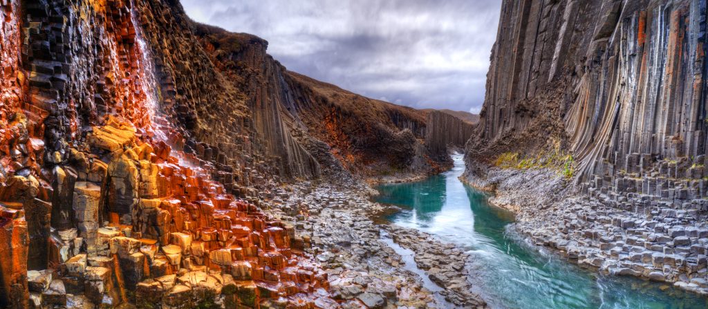 teal river flowing through gray, red, and orange basalt columns best things to do in Iceland