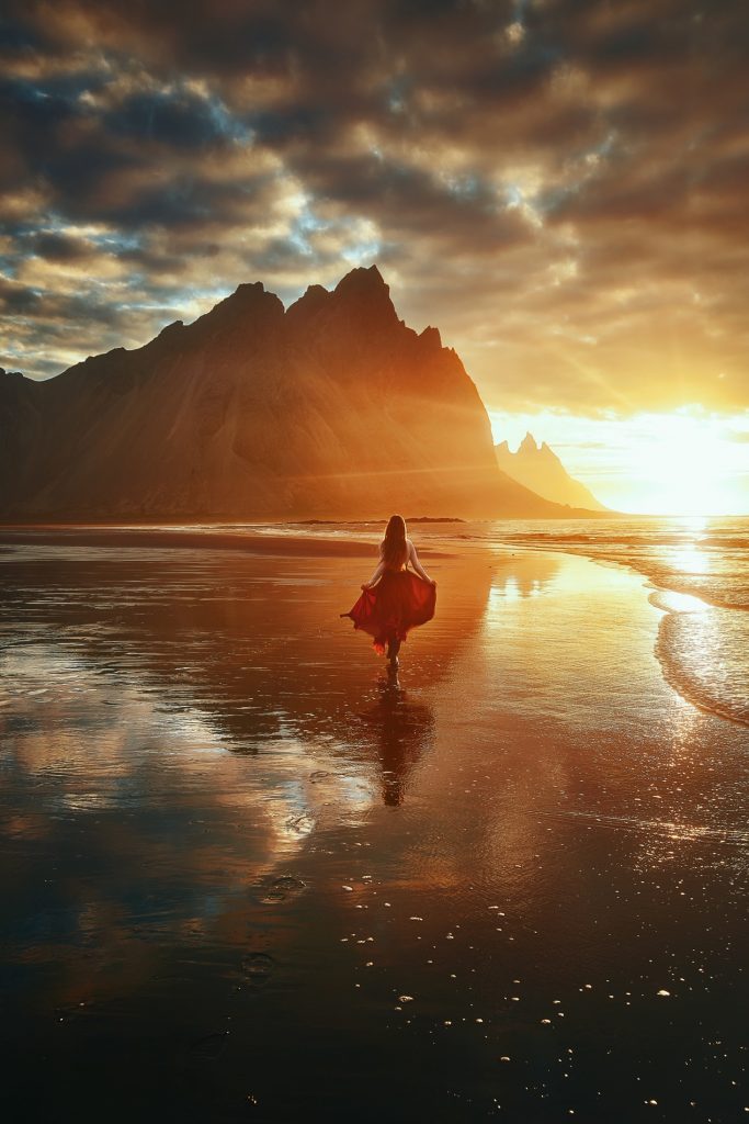 A woman prancing towards sharp Vestrahorn mountains during golden hour.