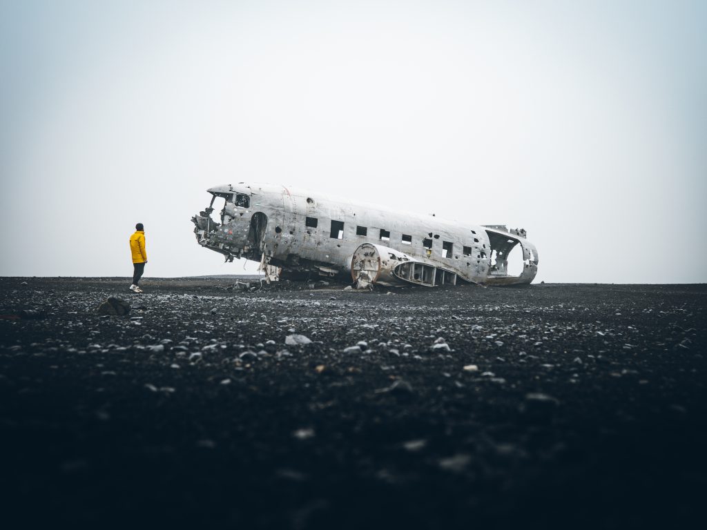 man in yellow looking at plane wreck on black sand best things to do in Iceland
