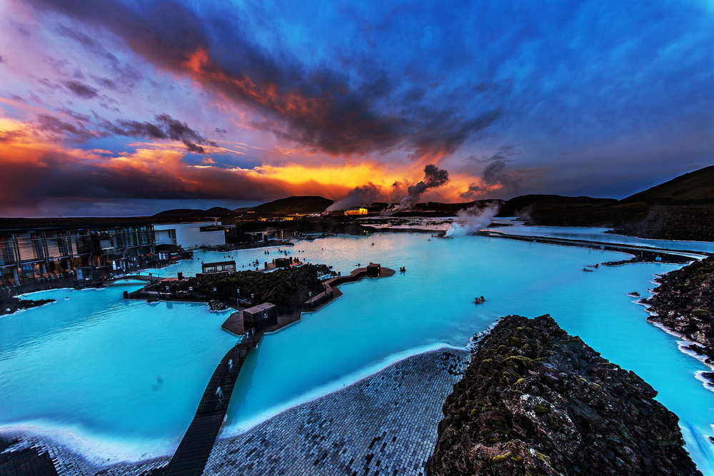 dramatic sunset behind the blue lagoon in Iceland with people swimming in it