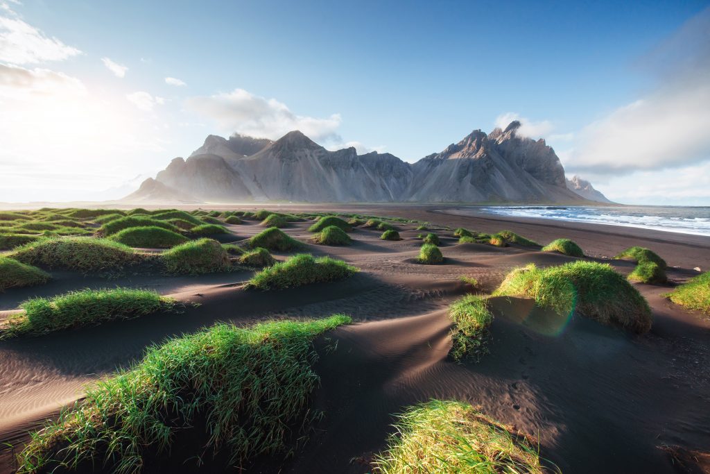 Photo of mountains and volcanic lava sand dunes on the beach in Stokksness, Iceland.