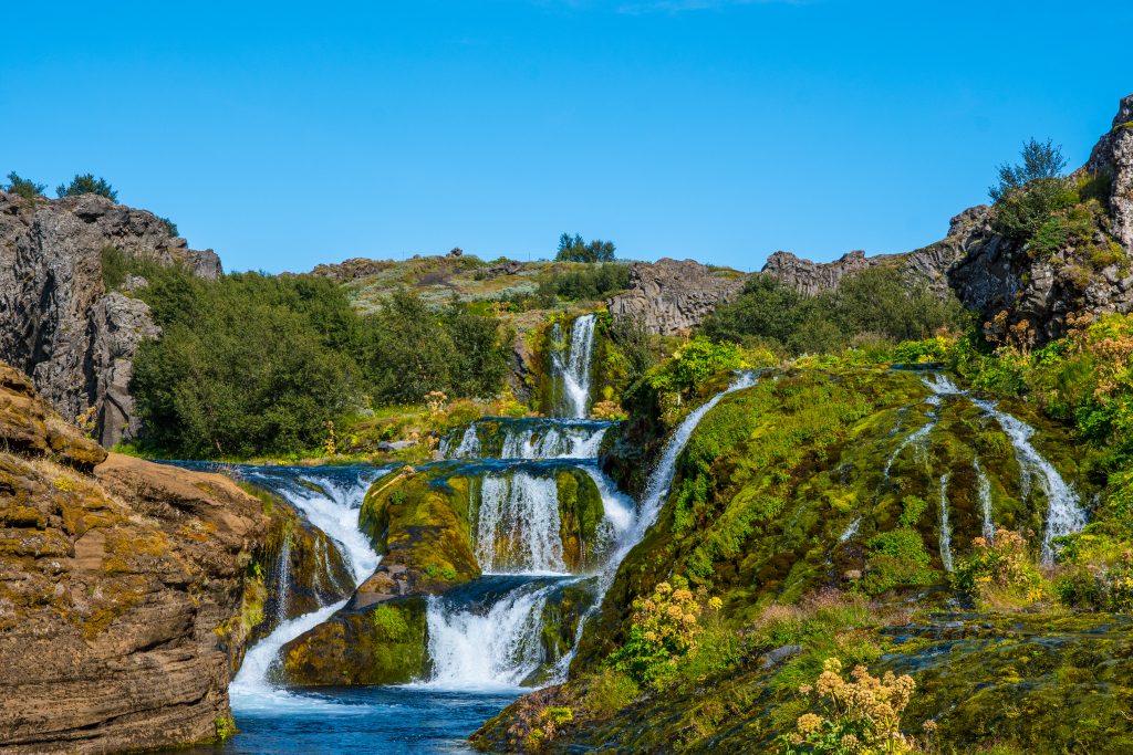 multi-layered waterfall cascading through greenery Iceland itinerary