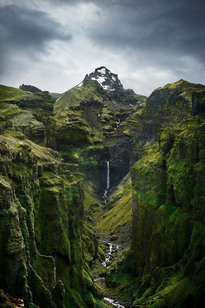 waterfall and river snaking through bright green and black canyon Iceland itinerary