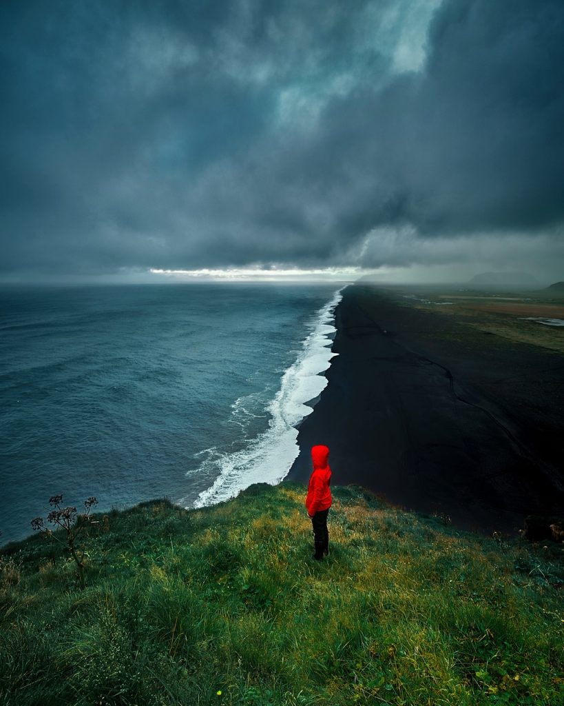 person in red raincoat staring at black sand beach coastline Iceland Itinerary