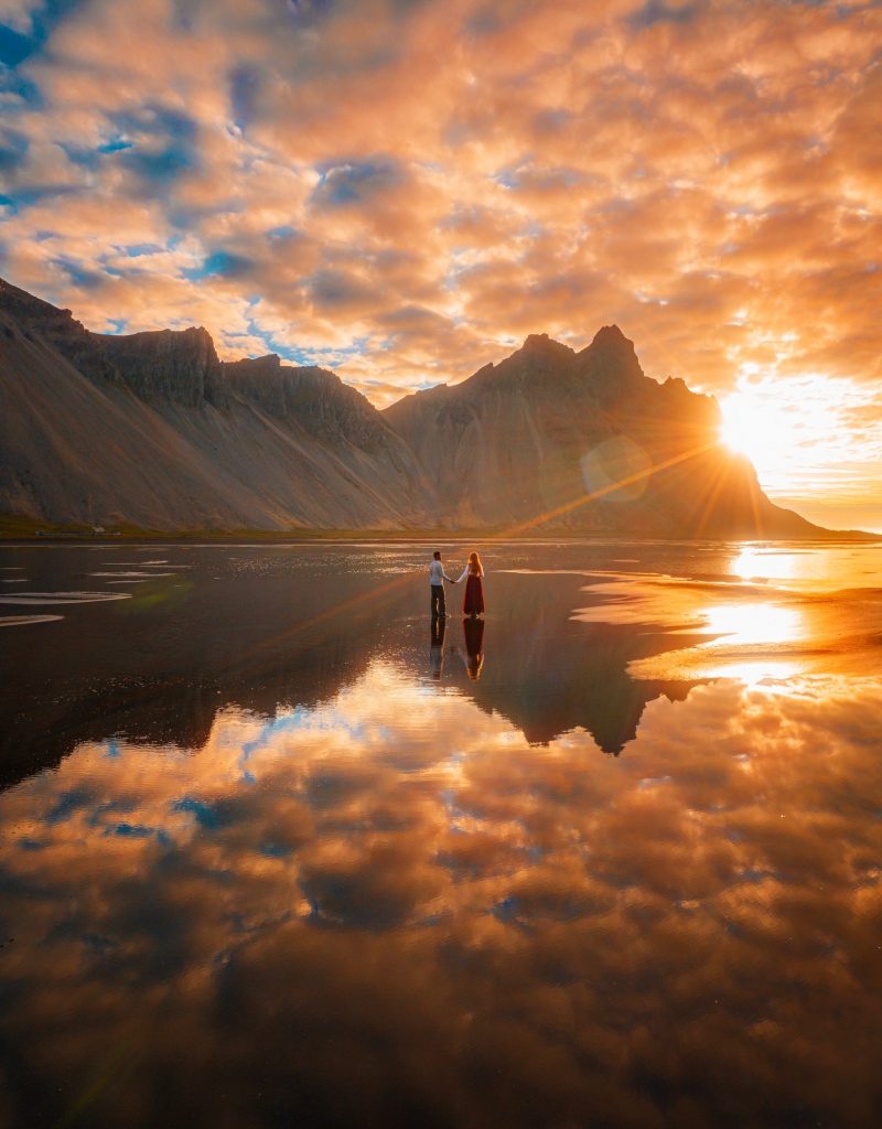 couple on reflective ground in front of towering mountains at golden hour