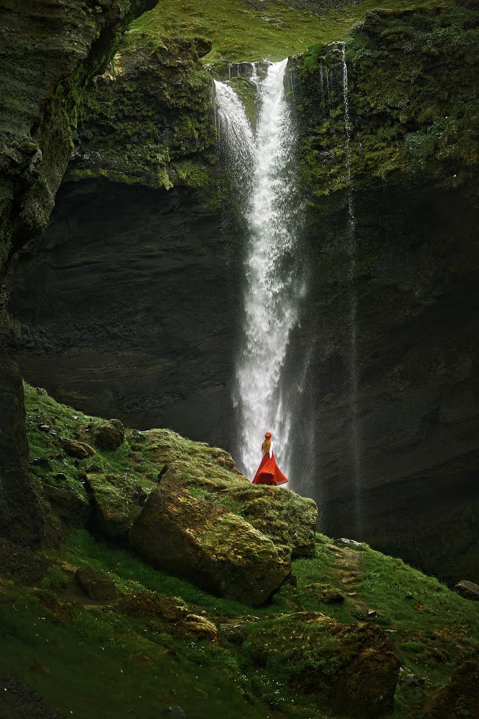 Woman in a long red skirt standing in front of Fagrifoss waterfall in Iceland