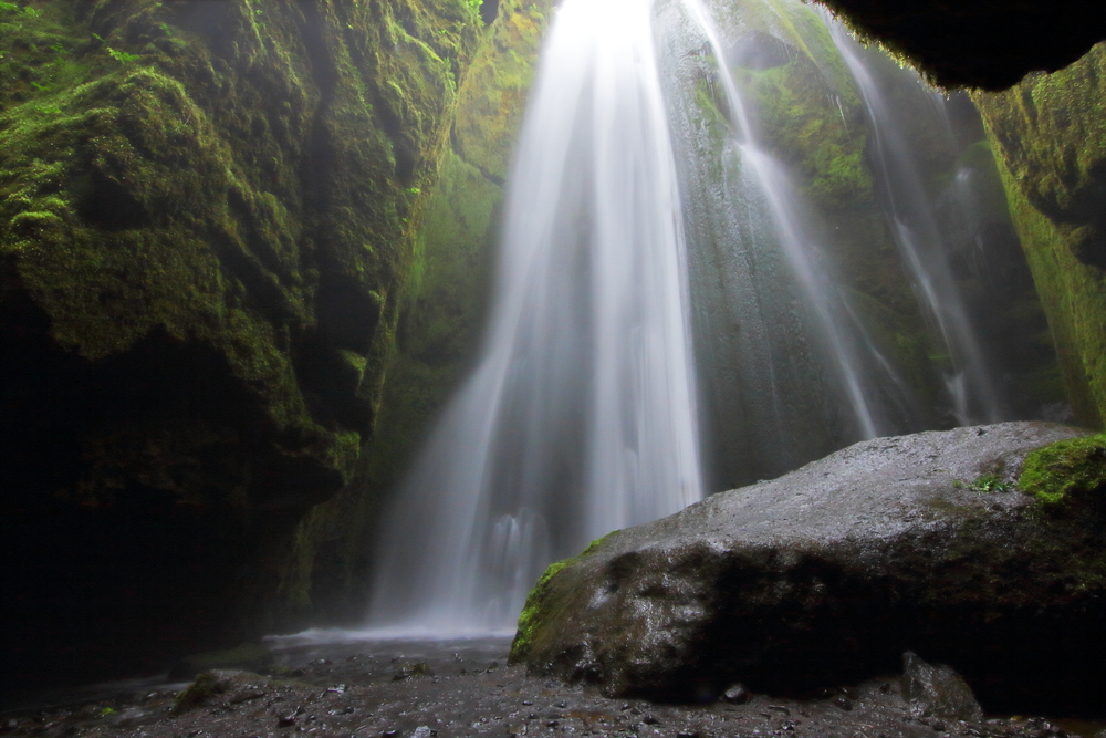 a waterfall flowing from above into a cave covered in moss