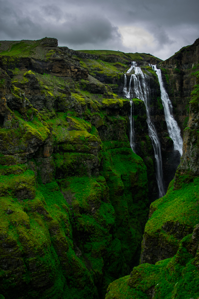 a deep green canyon with a large waterfall at the back.