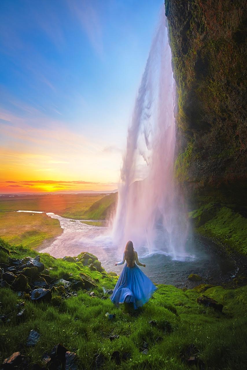 Woman in a blue dress standing in front of Seljalandsfoss at sunset