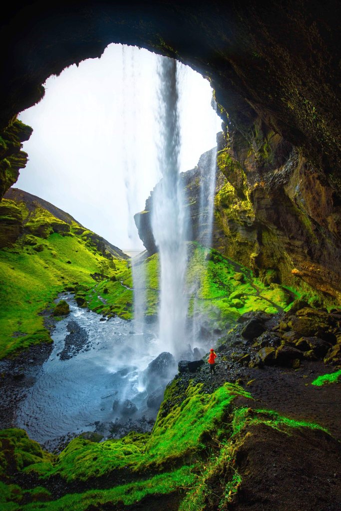 person walking behind Kvernufoss Waterfall in Iceland