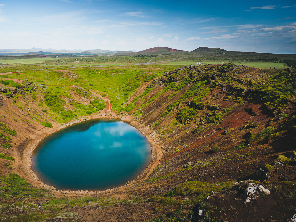 a crater filled with blue water in an open field on a sunny day