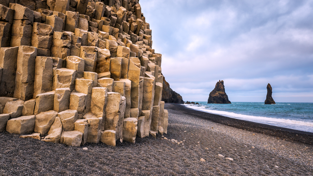 basalt rocks on a black sand beach in iceland with rock formations in the distance on a sunny day