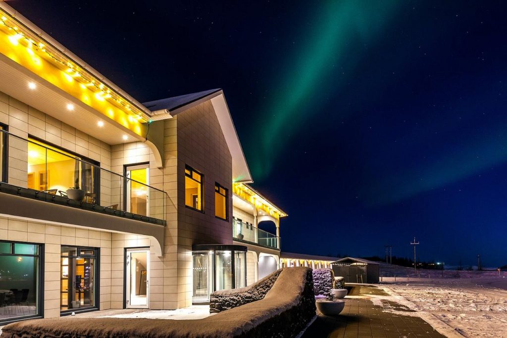 Exterior of Stracta Hotel Hella with lights on the building and the Northern Lights overhead.
