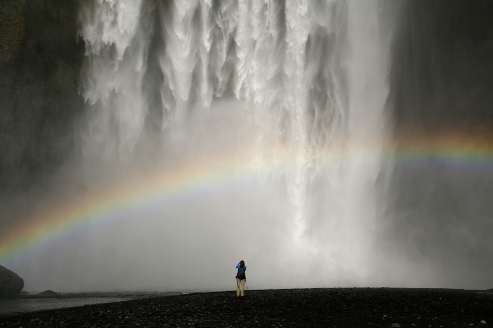Photo of someone standing in front of a waterfall in Iceland.