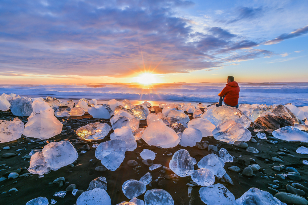 Man sitting on a block of ice at Iceland's glacier lagoon at sunset.