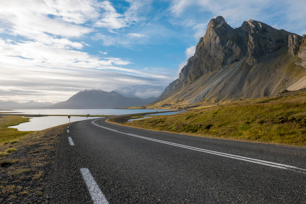 Photo of an Iceland road between water and cliffs.