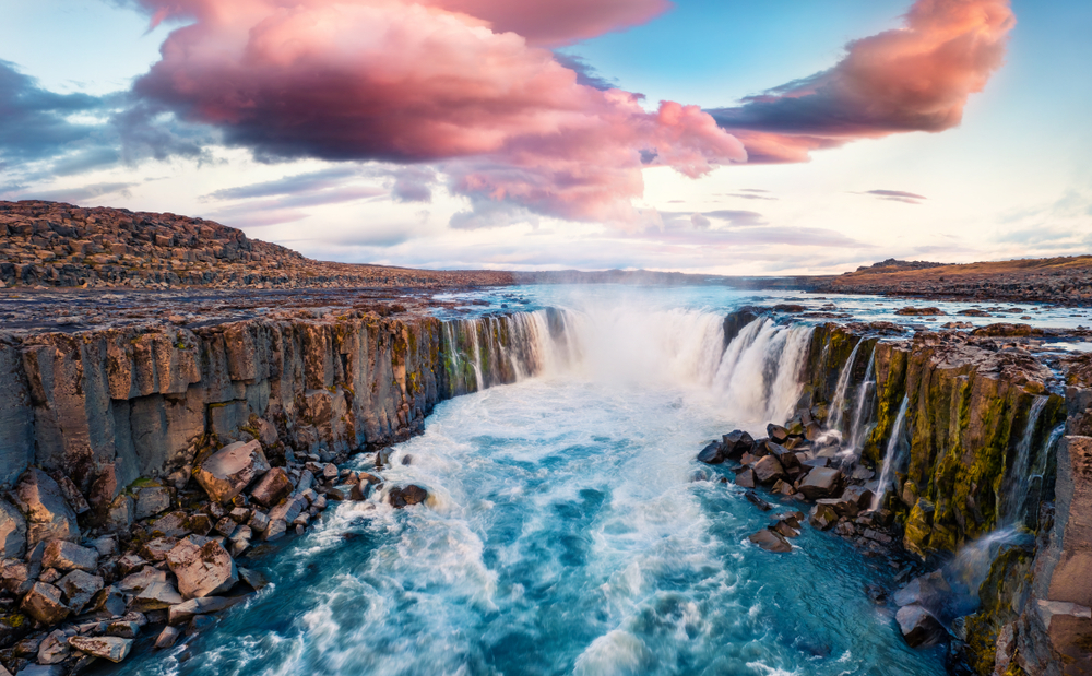 a waterfall flowing into raging river in a canyon at sunset