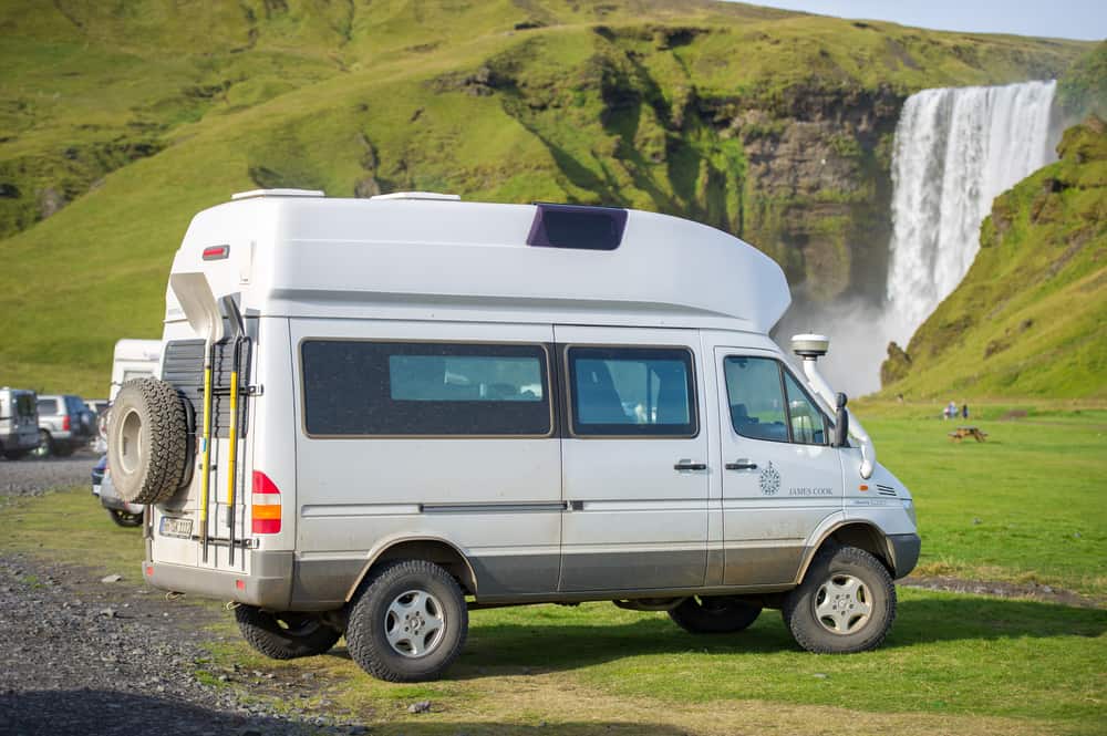 a camper van parked in grass with large waterfall in the background