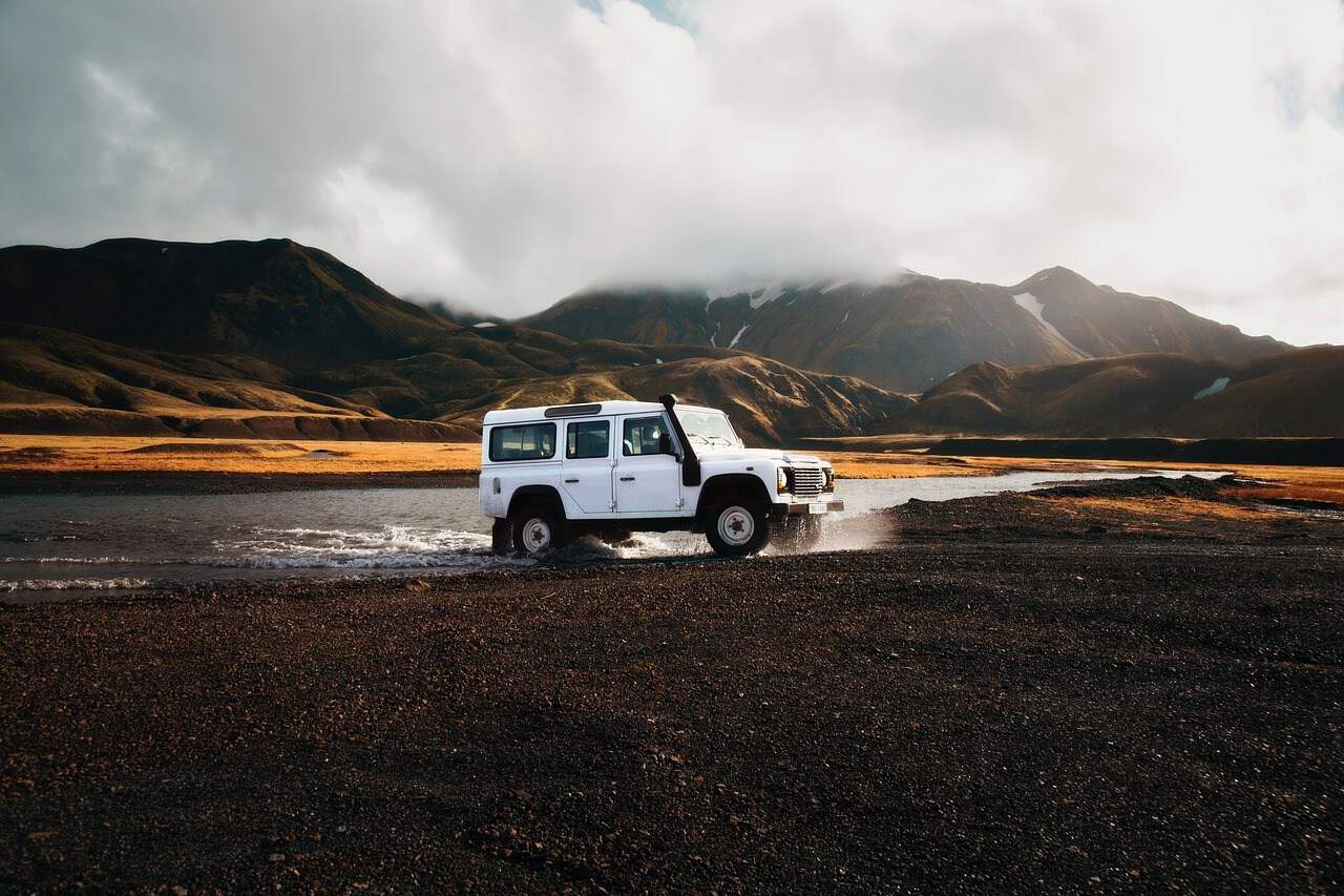 A white 4x4 truck forging a river with majestic landscape in the distance