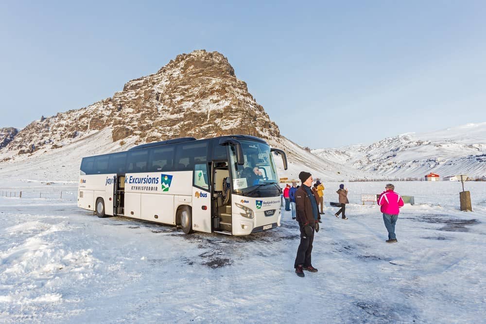 a tour bus stopped on snowy landscape with toursits walking around