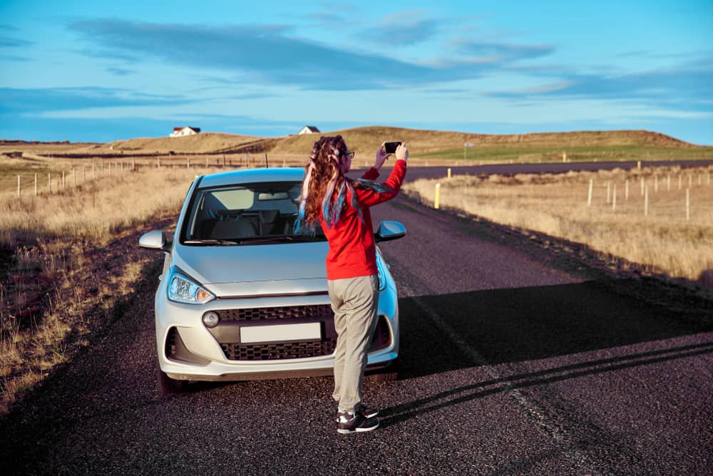 woman using phone for photos next to iceland car hire