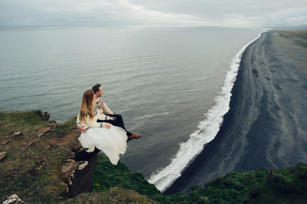 Photo of couple on a cliff in Iceland overlooking a beach.