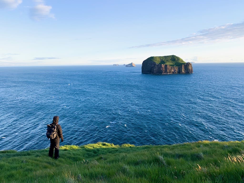 person standing on the windiest point in iceland looking out at a distant island. 