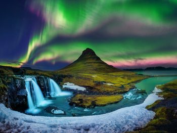 The Northern Lights framing a mountain with a waterfall in the foreground.