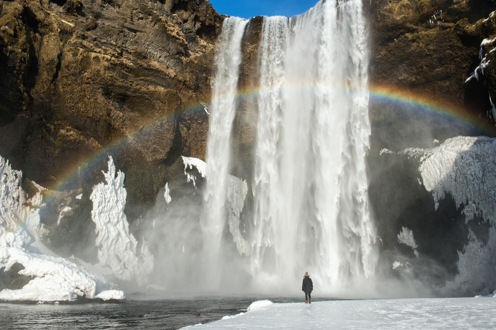 a person standing and looking at Skogafoss waterfall in Iceland in winter 