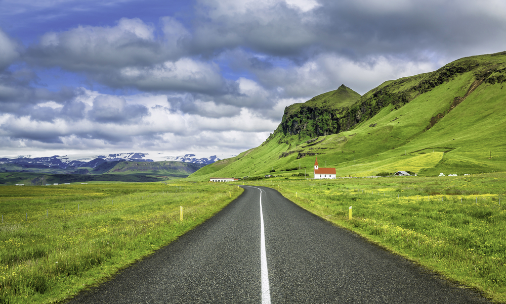 Road with beautiful green scenery and a church in the distance.