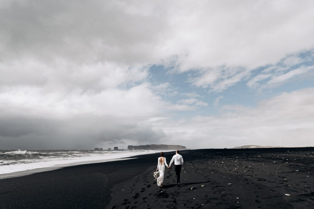 newly married couple walking down black sand beach together Iceland wedding