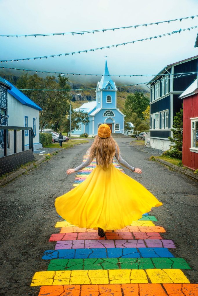 woman joyously skipping down rainbow street to adorable blue church