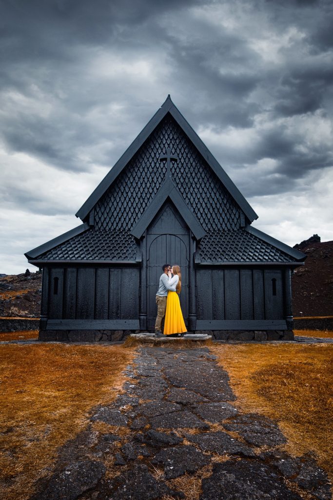 couple kissing in front of stark black church Iceland weddings